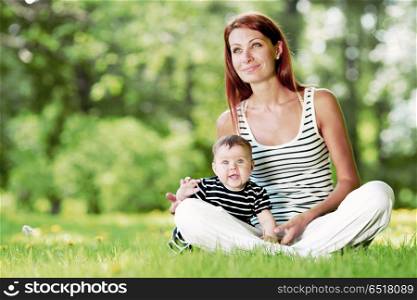Mother and daughter sitting on grass in spring park. Mother and daughter in park