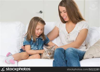 Mother and daughter sitting on sofa and cuddling cat