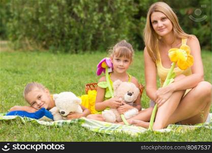 Mother and daughter sitting with soft toys on a picnic and watch the shot