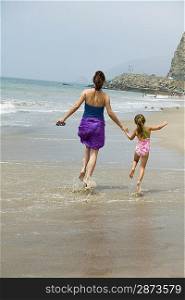 Mother and daughter skipping on beach