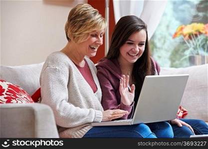 Mother and daughter smiling at laptop while using webcam