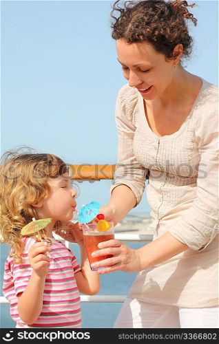 mother and daughter standing on cruise liner deck, mother holding cocktail in glass, daughter drinking it, vertical