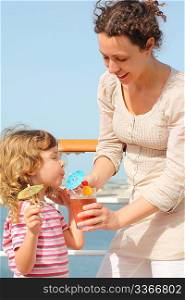 mother and daughter standing on cruise liner deck, mother holding cocktail in glass, daughter drinking it, vertical