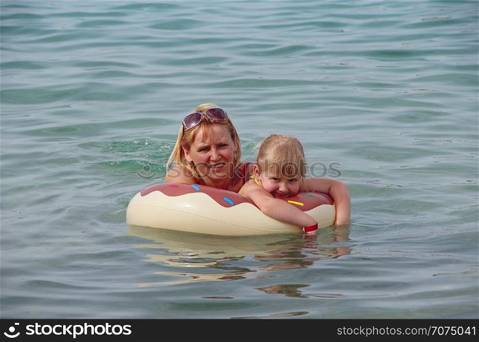 Mother and daughter swim in sea lying on inflatable circle in summer holidays. Rest on sea. Happy family in resort. Happy mother relaxing on rubber circle together with baby on sea during holidays. Mother and daughter swim in sea lying on inflatable circle in summer holidays