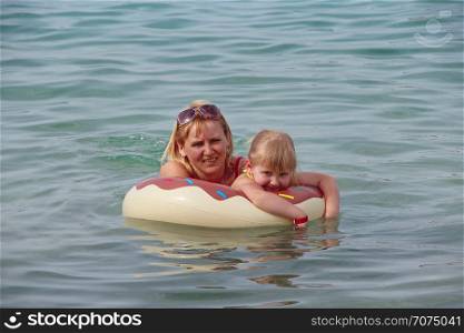 Mother and daughter swim in sea lying on inflatable circle in summer holidays. Rest on sea. Happy family in resort. Happy mother relaxing on rubber circle together with baby on sea during holidays. Mother and daughter swim in sea lying on inflatable circle in summer holidays