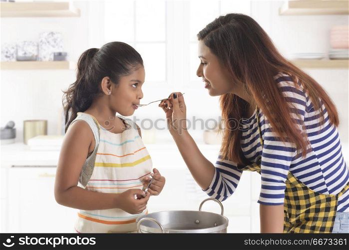 Mother and daughter tasting soup in kitchen