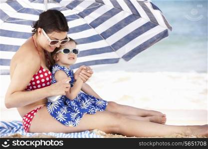 Mother And Daughter Under Beach Umbrella Putting On Sun Cream