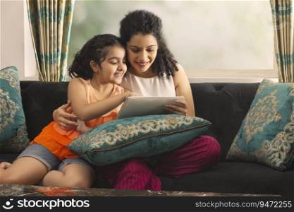 Mother and daughter using tablet together while sitting on sofa at home