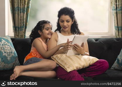 Mother and daughter using tablet together while sitting on sofa at home