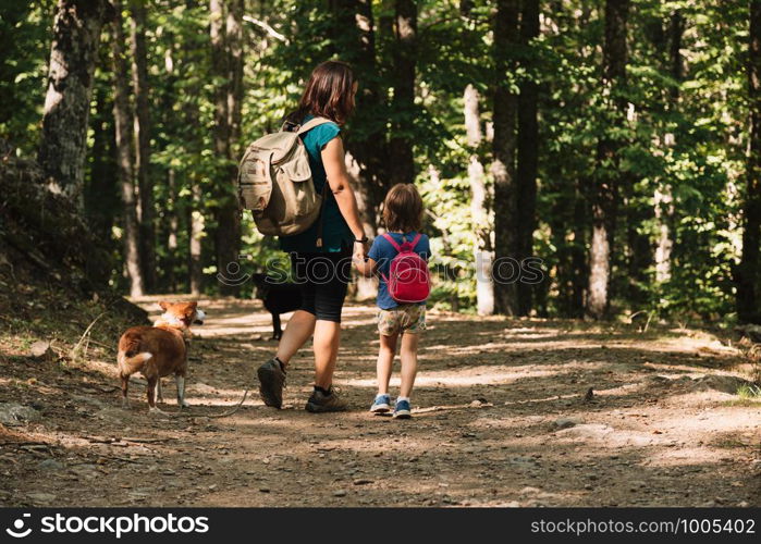 Mother and daughter walking trough a path with their dogs in the woods wearing backpacks and shorts