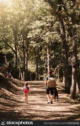 Mother and daughter walking trough a path with their dogs in the woods wearing backpacks and shorts