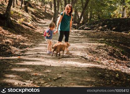 Mother and daughter walking trough a path with their dogs in the woods wearing backpacks and shorts