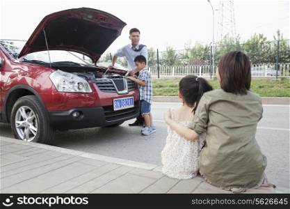 Mother and Daughter Watch as Father and Son Try to Fix the Car