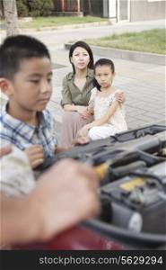 Mother and Daughter Watch as Father and Son Try to Fix the Car