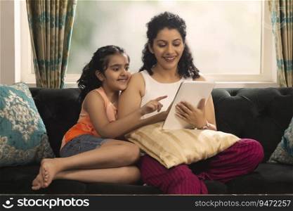 Mother and daughter watching tablet together while sitting on sofa at home
