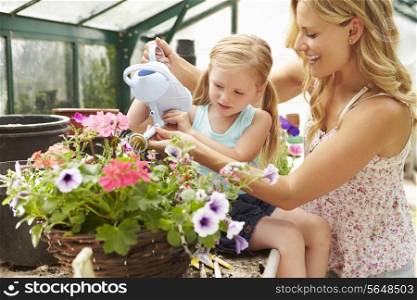 Mother And Daughter Watering Plants In Greenhouse