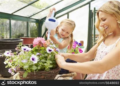 Mother And Daughter Watering Plants In Greenhouse