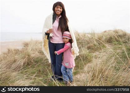 Mother And Daughter Wrapped In Blanket Amongst Dunes On Winter Beach