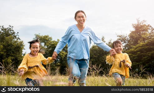 Mother and daughters holding hands and running on field in summer park. Happy family spend their free time together on vacation.
