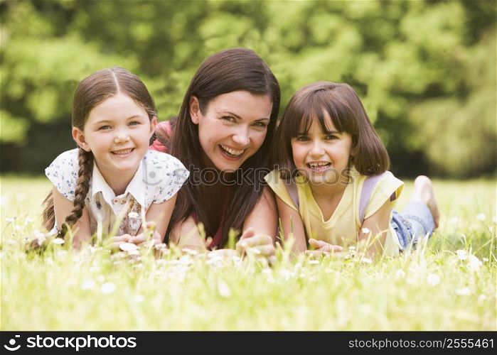 Mother and daughters lying outdoors with flower smiling