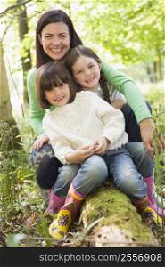 Mother and daughters outdoors in woods sitting on log smiling