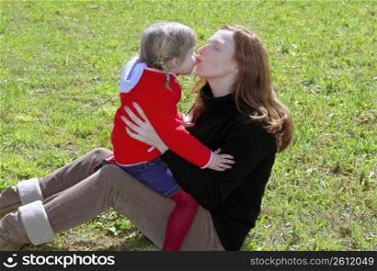 mother and daugther kissing mouth lips hug in winter meadow grass