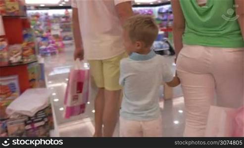 Mother and father holding son&acute;s hands while walking in toy shop