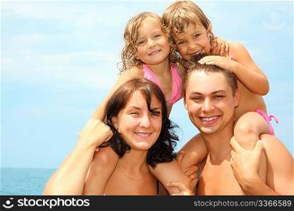 mother and father near water with two little girls sitting on their necks. they are cuddling.