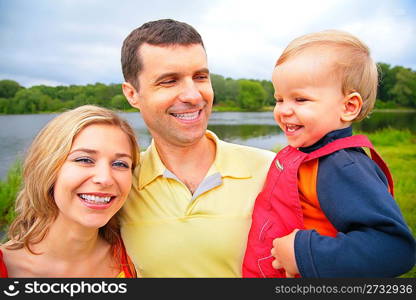 Mother and father with child on hands outdoors. wide angle.