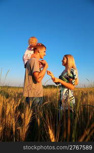 Mother and father with child on shoulders on wheaten field