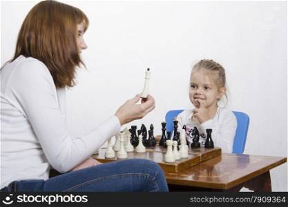 Mother and four-year-old daughter sitting at a table and play chess. Mom tells about the shapes