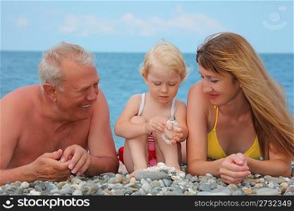 Mother and grandfather with child lie on sea coast