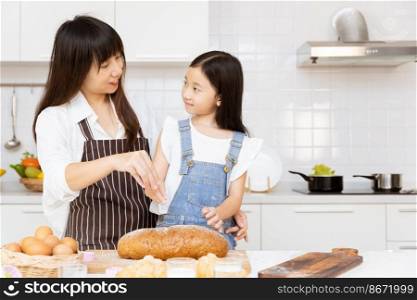 Mother and her child girl cooking food in home kitchen. Kid baking home made bread bun happy together with mom for holiday activity.
