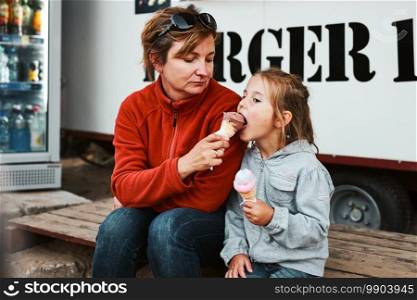 Mother and her daughter eating ice cream sitting on a step in front of food truck during summer vacations. Mother and her daughter eating ice cream sitting on a step in front of food truck
