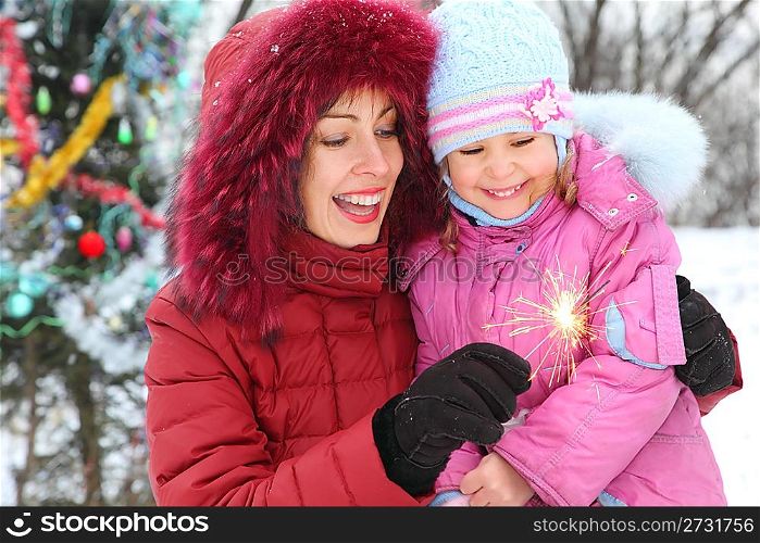 mother and her daughter wearing winter jacket is looking to bengal light. christmass three in out of focus.