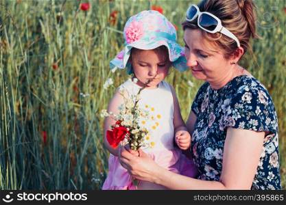 Mother and her little daughter in the field of wild flowers. Little girl picking the spring flowers for her mom for Mother?s Day in the meadow. Nature scene, family time
