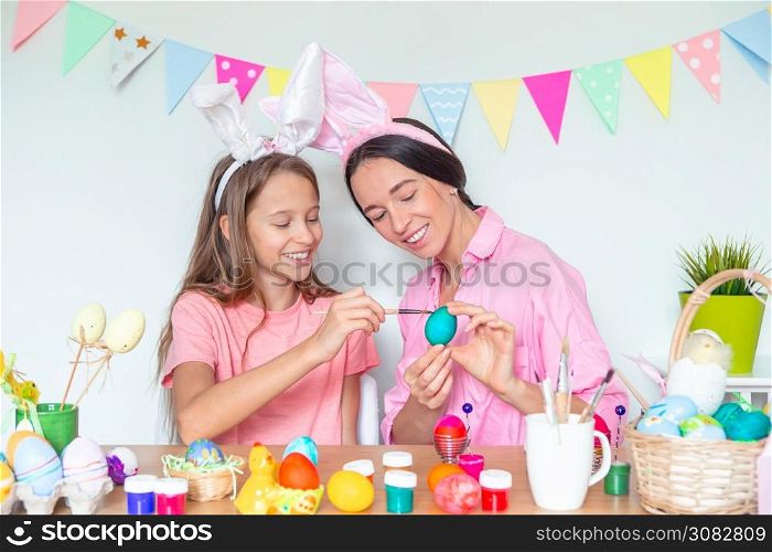 Mother and her little daughter painting eggs preparing for Easter. Family wearing bunny ears at home. Mother and her little daughter painting eggs. Happy family preparing for Easter.
