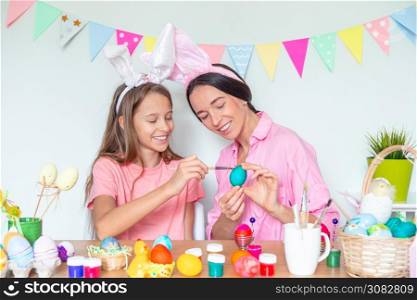 Mother and her little daughter painting eggs preparing for Easter. Family wearing bunny ears at home. Mother and her little daughter painting eggs. Happy family preparing for Easter.