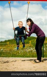 Mother and her little son having fun together at the playground. Child kid playing on a swing. Happy healthy childhood.