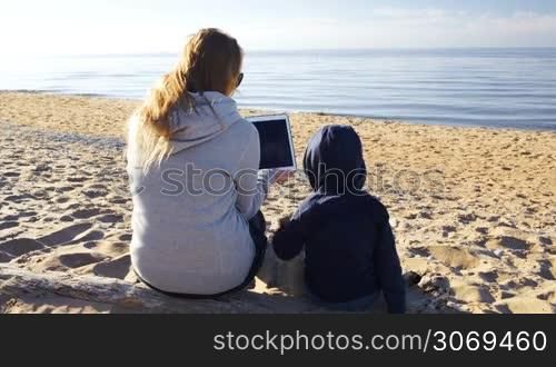 Mother and her little son on the beach. Boy touching the screen of tablet PC held by mother