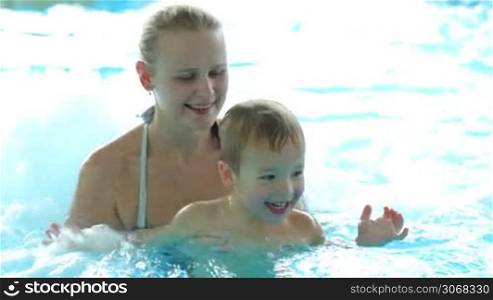 Mother and her little son playing in rough water of the pool. Family fun in waterpark.