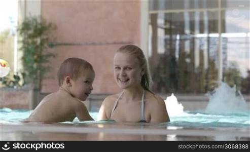 Mother and her little son playing in rough water of the swimming pool. Family fun in waterpark.