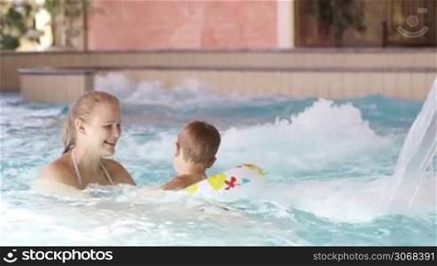 Mother and her little son with floating ring swimming in rough water of the pool. Family fun in waterpark.