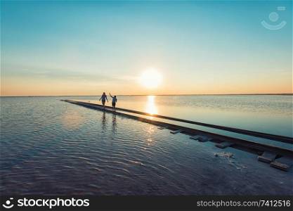 Mother and her son walking on railway in salty lake. Beauty sunset on salty lake in Altay, Siberia, Russia. Beauty sunset on salty lake