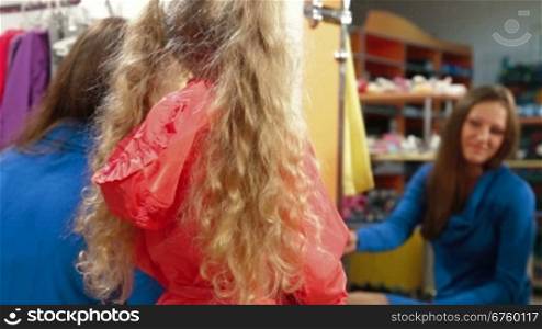 Mother and little daughter shopping for girls clothes in a clothing store, trying on raincoat