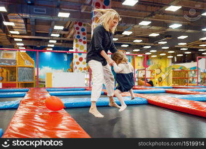 Mother and little girl jumping on a trampoline in the entertainment center. Mom and her daughter leisures on holidays, childhood happiness, happy kids on playground. Mother and little girl jumping on a trampoline