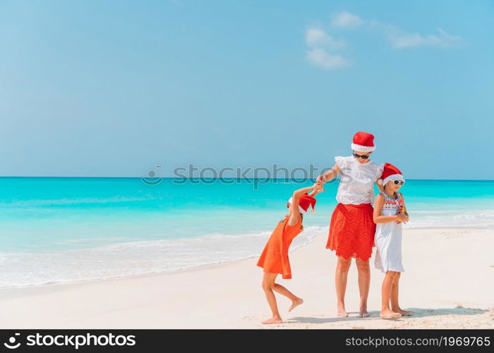 Mother and little girls on vacation on the beach having fun on Christmas vacation. Adorable little girls and young mother on tropical white beach on Christmas vacation