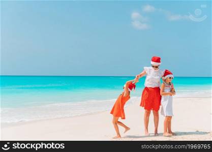 Mother and little girls on vacation on the beach having fun on Christmas vacation. Adorable little girls and young mother on tropical white beach on Christmas vacation