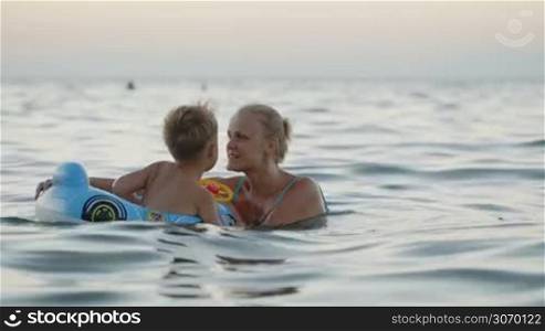 Mother and little son enjoying playing in the sea. Woman spinning excited boy in rubber ring. Family fun during summer vacation