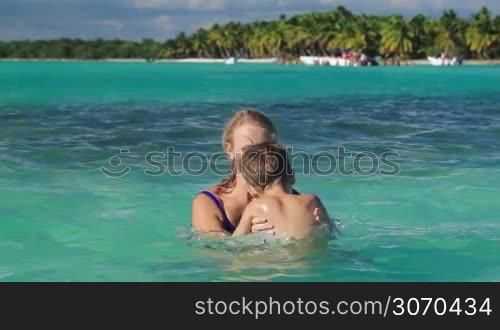 Mother and little son having fun in clear blue sea on tropical resort. Mom dousing boy and then taking him up. Summer vacation